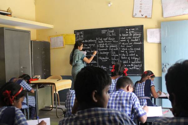 A teacher writes on the blackboard as pupils work at their desks